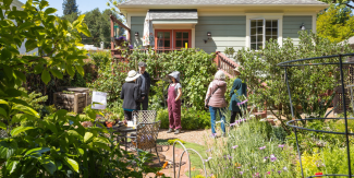 People stand around a residential garden full of various plant varieties. 