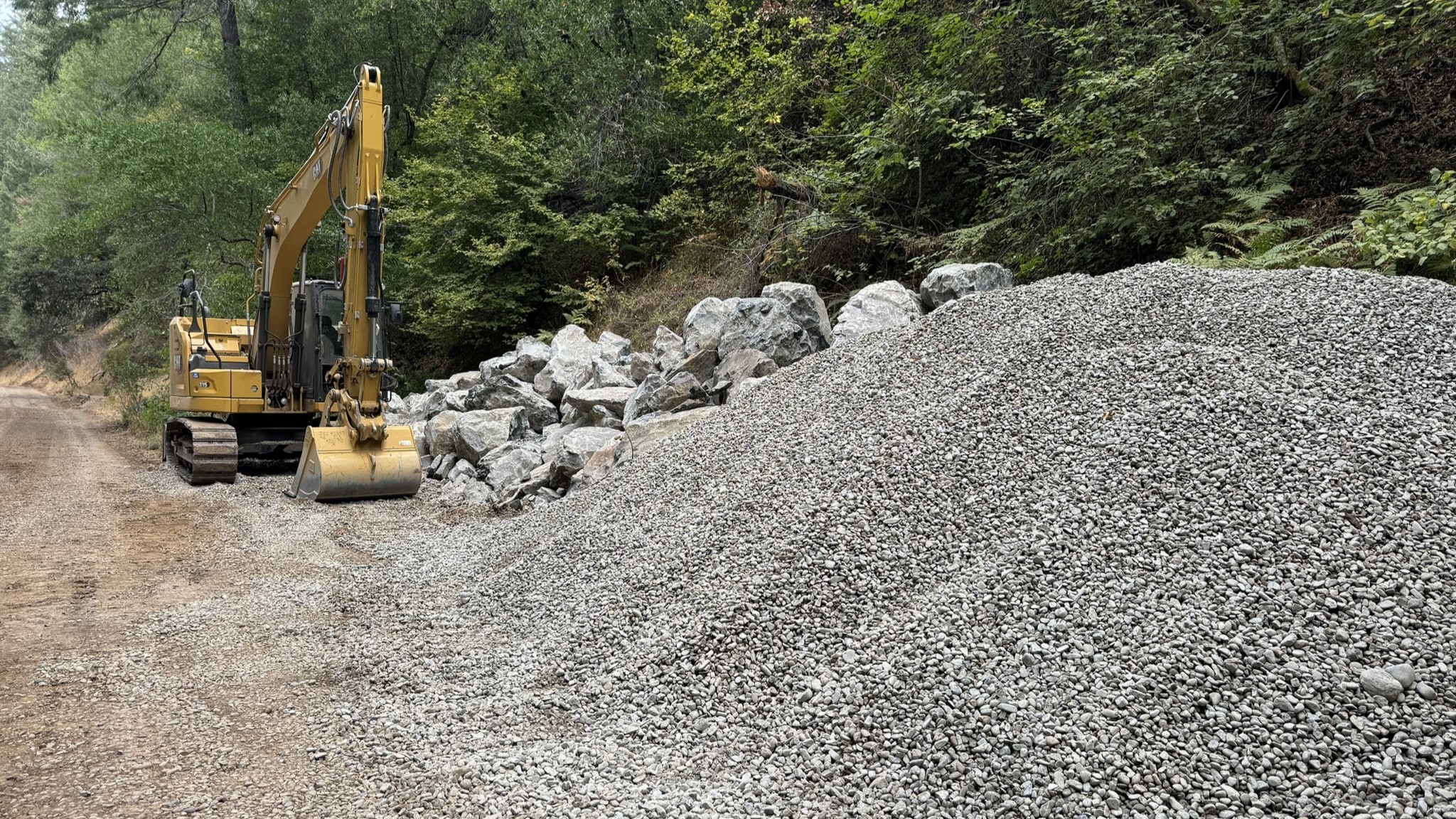 A large pile of gravel and boulders next to heavy construction equipment