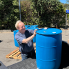 A person loads a blue barrel into the back of a truck.