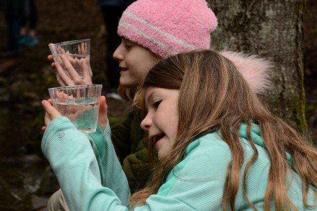 Two children look at small fish in water cups. 