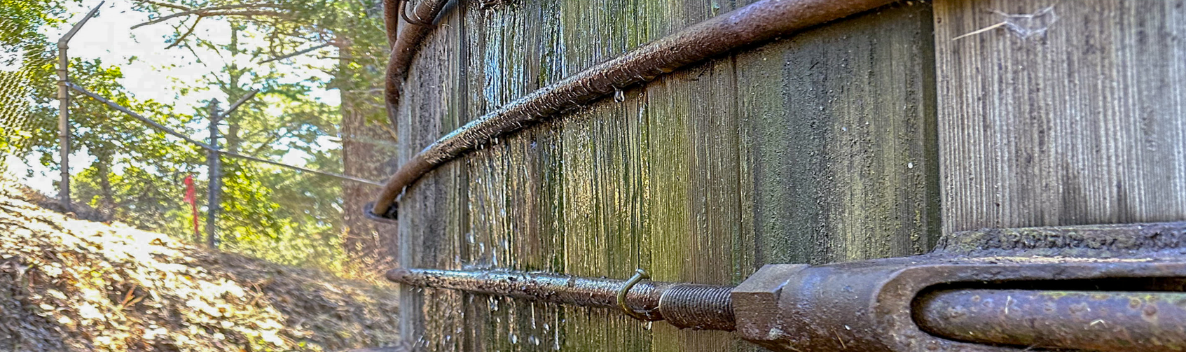 Water drips past metal belts wrapped around redwood slats as part of a massive water storage tank. 