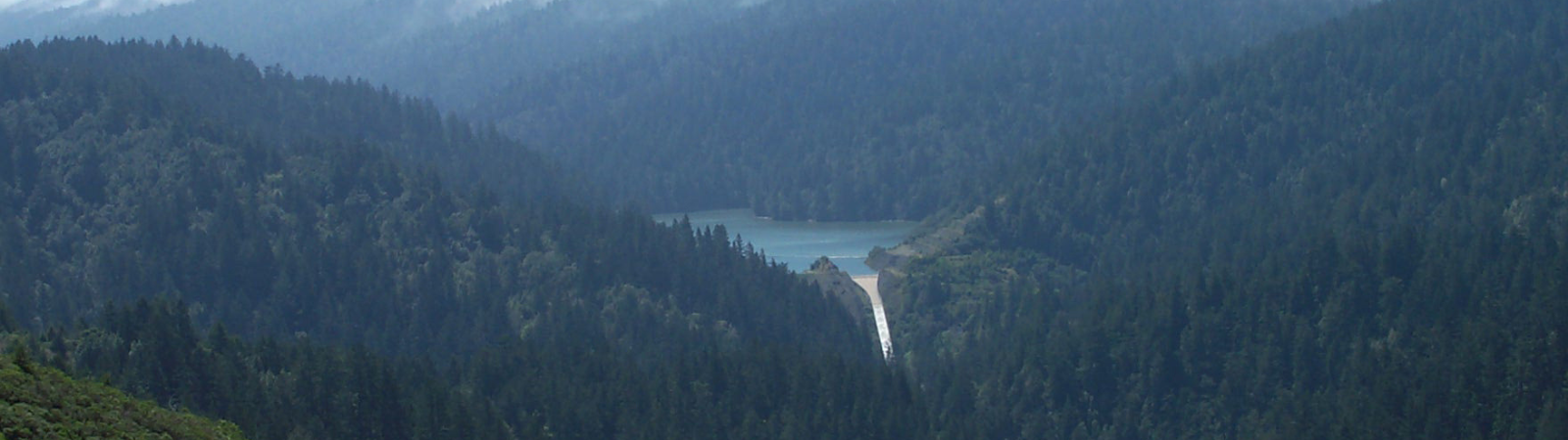 A spillway from a dam surrounded by tree-covered mountains.