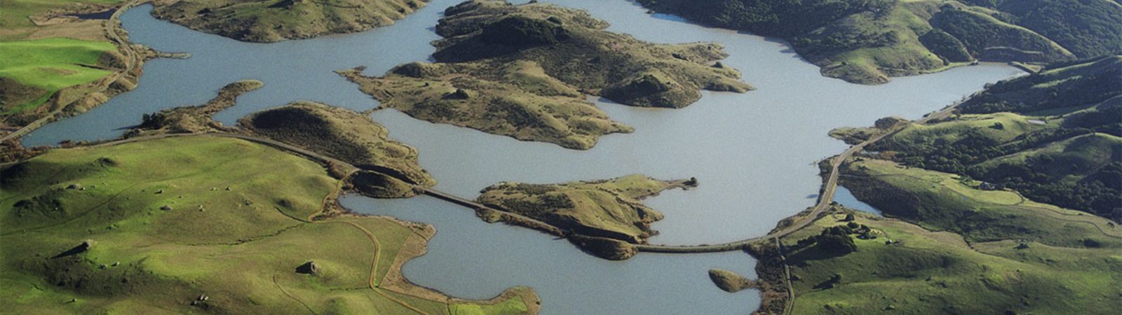 Aerial image shows a lake surrounded by green hills. 