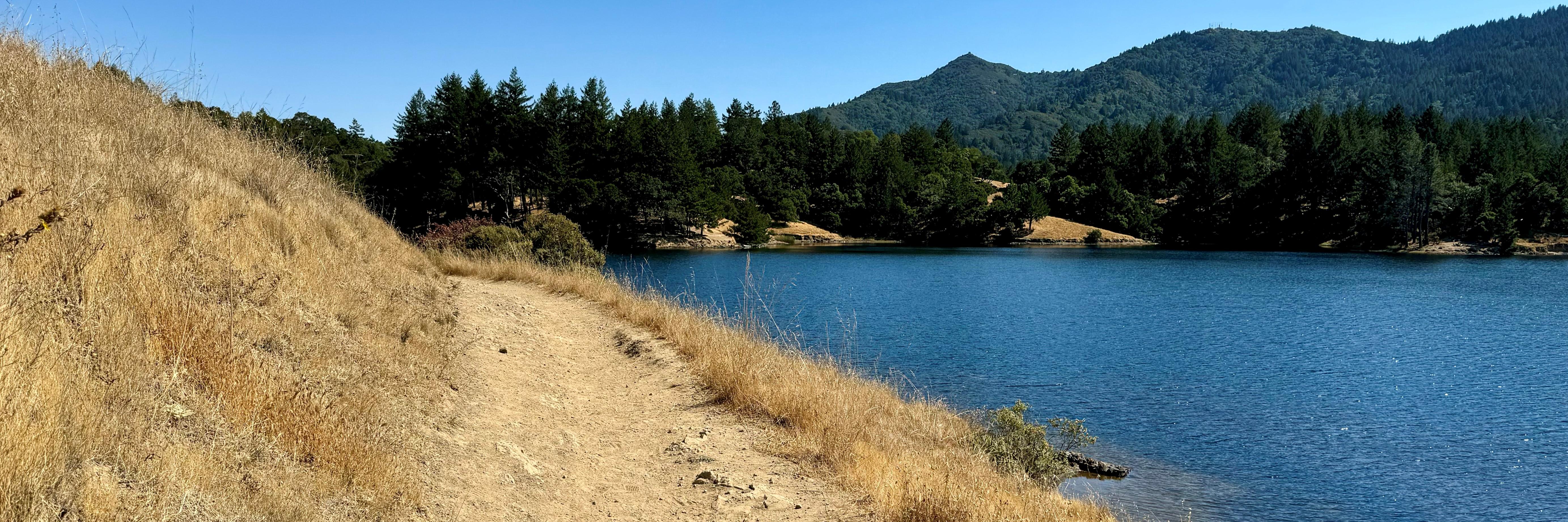 A trail along a grassy hillside and reservoir with Mt. Tamalpais in the background