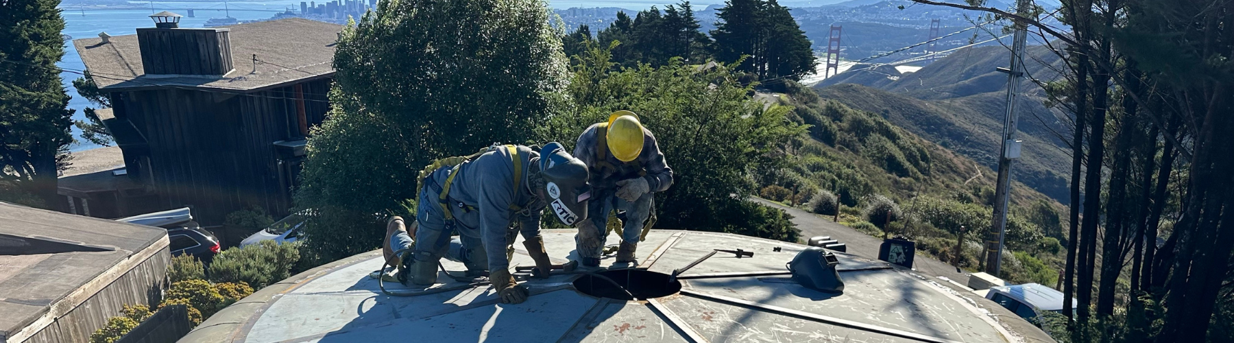 Two workers inspect a water tank high atop a hillside.