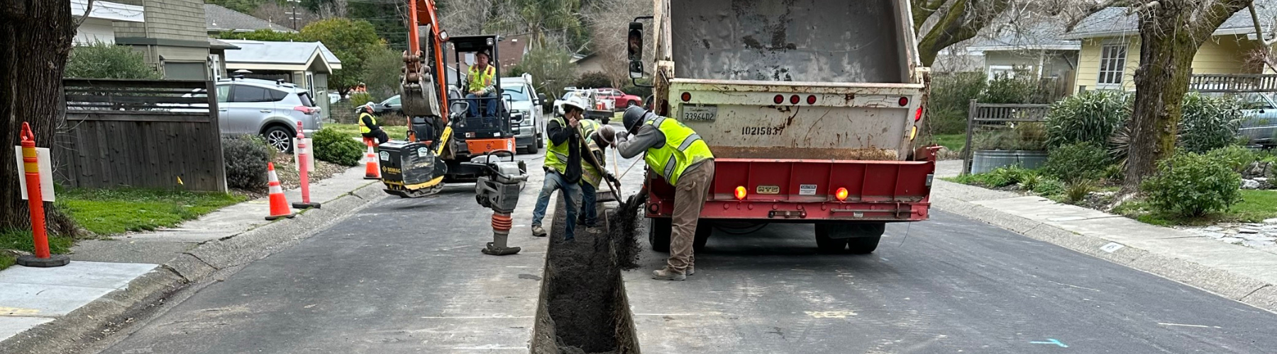 Workers work around a trench in a residential roadway.