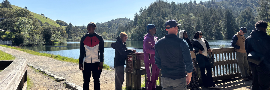 People stand and look out on a reservoir surrounded by tree-covered hillsides.