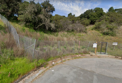 A street next to a hillside with a fence and trees