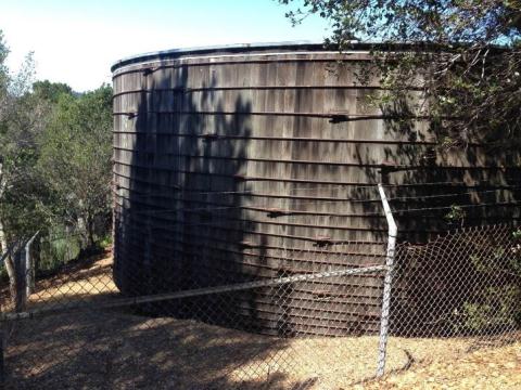 Redwood water storage tank behind a chainlink fence