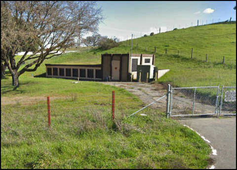 Pump station, road, and fence, surrounded by grass