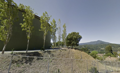 Water tank lined with trees on a hillside behind a chainlink fence