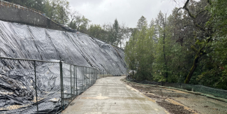 Photo shows a hillside covered in tarps and surrounded by a tall chain-link fence. 