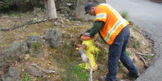 A man in a safety vest stands over a fire hydrant
