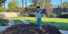 A boy raises his arm while standing on top of a pile of compost.