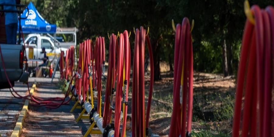 A row of red hoses stretch out at the edge of a parking lot. 