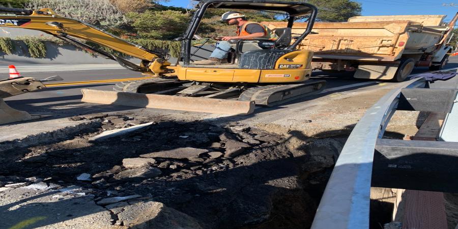 A person operates a small backhoe next in a roadway. 