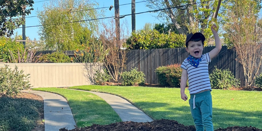 A boy raises his arm while standing on top of a pile of compost.