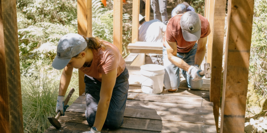 People work on a small wooden bridge in a remote, wilderness setting.